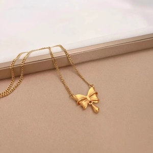 Collier nœud doré avec pendentif goutte d'eau sur fond de satin beige chaud
