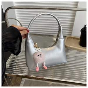 Close-up of a silver metallic hobo bag with a firm handle and a cute pink plush charm