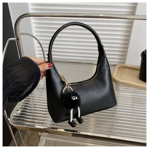 Close-up of minimalist black underarm bag with a fluffy cartoon charm and matte leather texture