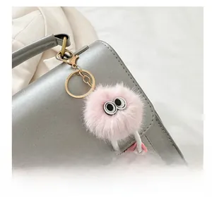 Close-up of a pink fuzzy monster bag charm with big eyes and metal clasp on a grey bag