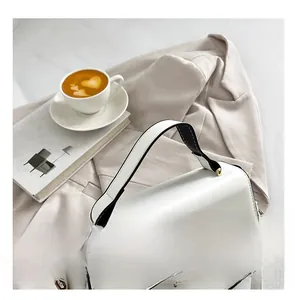Close-up of white leather handbag with gold twist lock and black edge finish