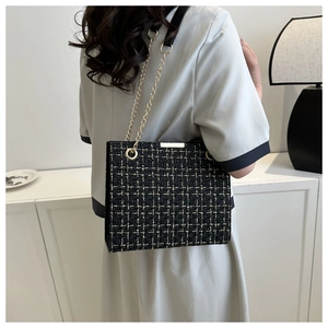 Detail of tweed crossbody bag with black-gold weave and elegant chain strap on shoulder