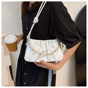Detail of white pleated cloud bag featuring elegant pearl and gold flower chain strap