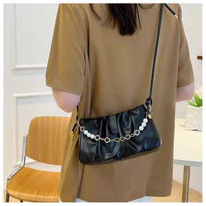 Detail of black pleated shoulder bag featuring elegant pearl and gold flower chain strap