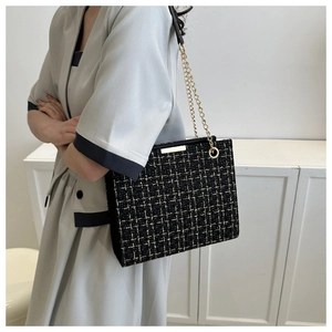 Detail of elegant black tweed shoulder bag with gold chain and woven texture finish