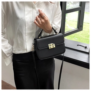 Close-up of elegant black leather square bag with premium gold rotating metal lock detail