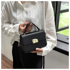 Detail of black faux leather handbag featuring a golden cross-shaped lock and sturdy handle