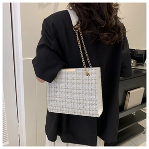 Rear view of a model wearing a tweed tote bag with gold chain strap in a modern office setting
