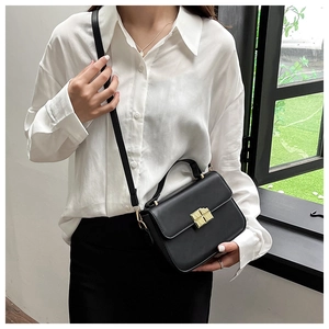 Detail of a black leather crossbody bag featuring a classic gold rectangular twist lock