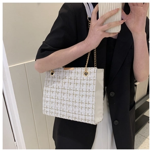 Detail of tweed crossbody bag with gold chain and metal buckle on black suit jacket