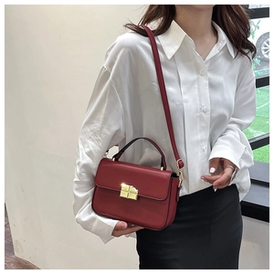 Detail shot of vintage style wine red crossbody bag with golden metal buckle on white shirt