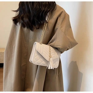 Quilted beige crossbody bag with gold chain strap and tassel detail on a brown coat