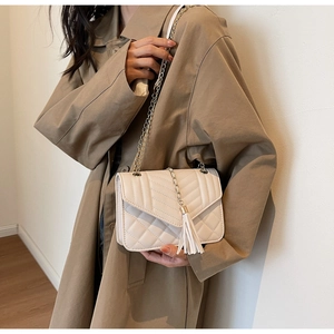Detail of cream quilted chain bag with tassel pendant worn with khaki coat