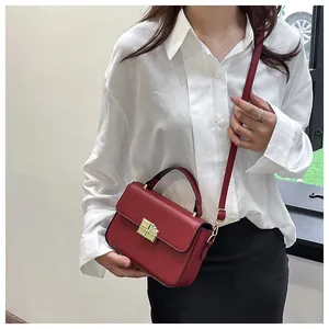 Detail of red leather crossbody bag with golden square clasp and adjustable shoulder strap
