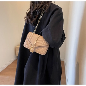 Detail of beige quilted shoulder bag with gold chain strap and tassel on model