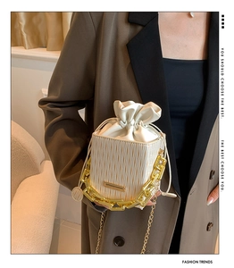 Detail of cream white pleated bucket bag with dual gold chain straps and drawstring