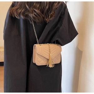 Close-up of beige quilted crossbody bag with tassel detail and gold chain strap