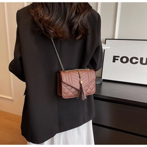 Detailed shot of dark brown quilted crossbody bag with gold chain strap and tassel