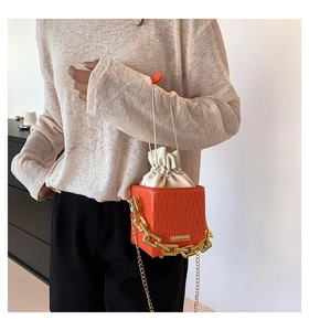 Close-up of orange textured box bag with chunky gold chain and drawstring liner