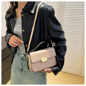 Close-up of nude beige square handbag with gold metal lock worn with a leather jacket