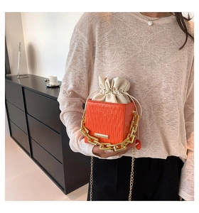 Detail of orange quilted crossbody bag featuring a chunky gold chain and drawstring inner