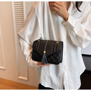 Close-up of black quilted shoulder bag featuring V-shaped stitching and leather tassels