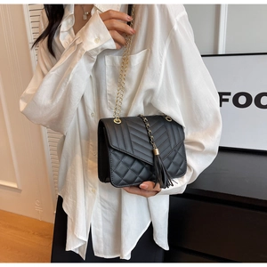 Detail of a black quilted leather crossbody bag with gold chain strap and tassel