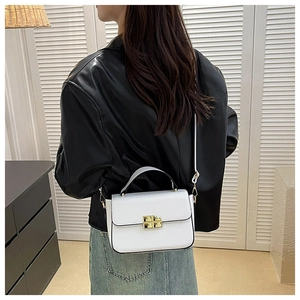 Detailed view of a white leather crossbody bag with a gold metal lock worn by a model