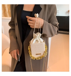 Close-up of white pleated bucket bag with gold chain and heart drawstring detail