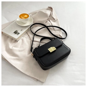Detail view of a black vintage crossbody bag with a gold metal lock on a beige blazer
