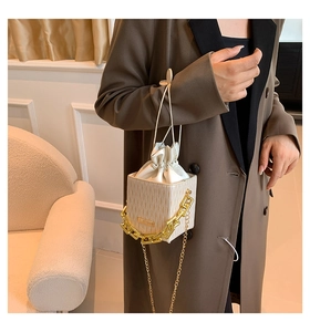 Detail of cream crossbody bag featuring vertical stripe texture and chunky gold chain