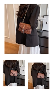 Detail of brown quilted crossbody bag with tassel pendant and gold chain strap