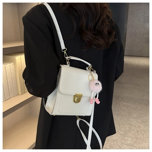 Dettaglio di un mini zaino in pelle bianca con chiusura dorata e pompon rosa soffice