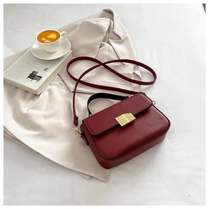 Detail of burgundy leather handbag with gold lock placed on a stylish beige blazer