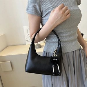 Minimalist black leather crescent underarm bag with cute monster plush charm on a model