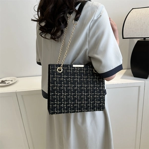 Classic black and gold tweed shoulder bag with chain strap worn by a model in interior