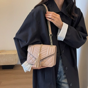 Quilted beige crossbody bag with V-shaped flap, metal chain, and stylish tassel accent