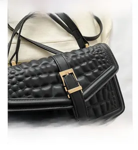 Detail shot of black faux leather handbag showing crocodile texture and gold metal buckle