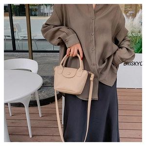 Detailed shot of beige lychee pattern bucket bag with round buckle and slim shoulder strap