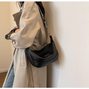 Détail du sac demi-lune en cuir noir avec bandoulière à lettres porté par un mannequin