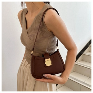 Détail d'un sac selle en cuir marron avec boucle dorée sur un modèle en maille beige