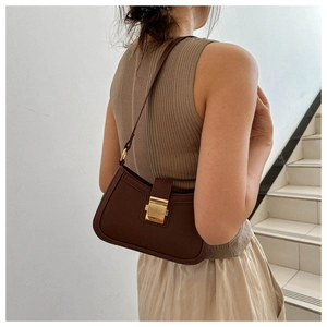 Gros plan du sac sous le bras en cuir marron avec fermoir doré sur l'épaule du modèle