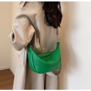 Sac bandoulière demi-lune vert avec texture litchi porté par un mannequin en trench beige