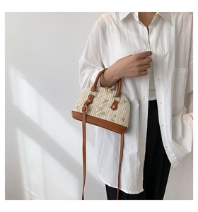 Close-up of shell-shaped straw bag with floral embroidery and brown leather trim details