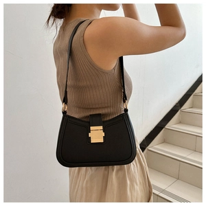 Détail d'un sac sous le bras en cuir noir avec boucle dorée porté par un mannequin