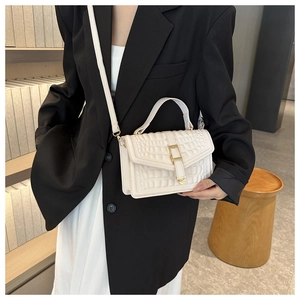 Detailed view of white crocodile pattern leather handbag with gold metal clasp on a model