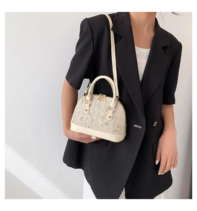 Detail of shell-shaped straw bag featuring delicate floral embroidery and leather handles