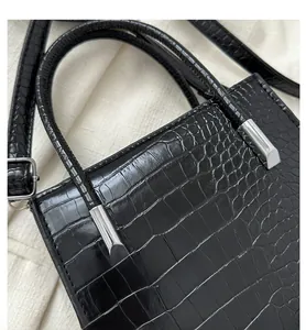 Detail of black crocodile texture handbag with silver metal buckles and adjustable strap