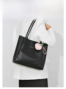 Détail du sac cabas noir gaufré avec bandoulière tissée et charm pêche en peluche rose