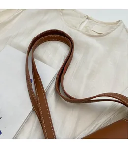 Detail of a brown leather shoulder strap with visible white stitching and smooth finish